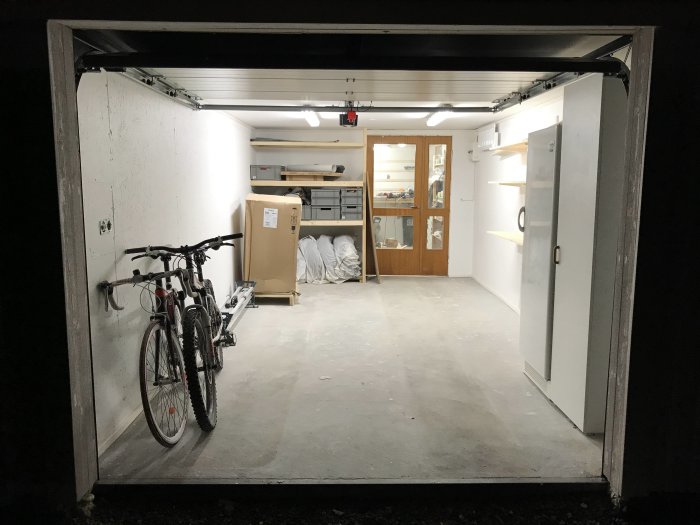 Interiör av garage med ny monterad garageport, upplyst arbetsbänk, cykel och dörr i bakgrunden.