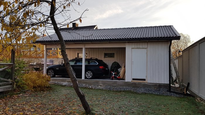 Bil parkerad under en smal carport med grusad uppfart och trädäck bredvid.