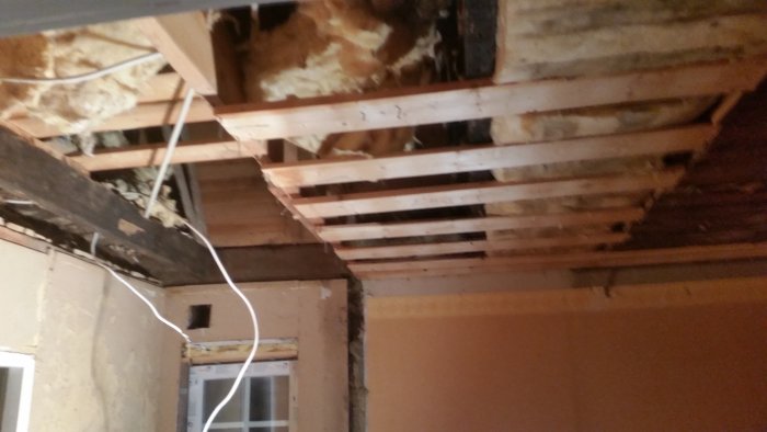 Avlägsnade takbrädor visar isolering och takbjälkar i ett pågående renoveringsprojekt.