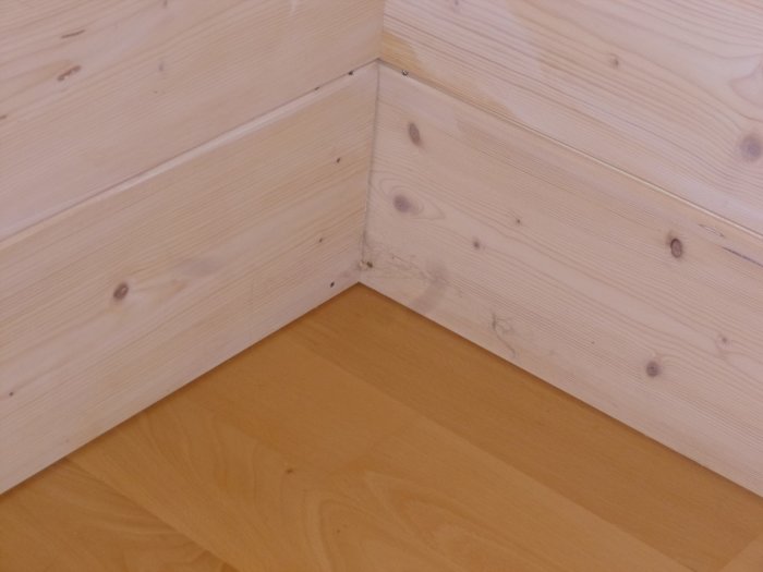 En vitvaxad väggpanel med 2-3 mm shadow gap ovanför ett ljust bokgolv i ett hem.