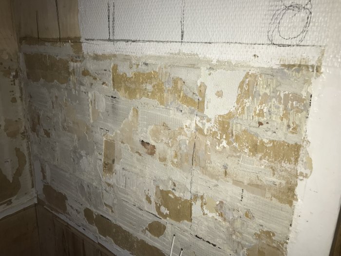 Vägg med borttaget kakel och synlig plyfaskiva samt rester av kakelfix och spackel.