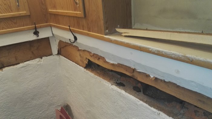 Delvis isärmonterad källartrappa med masonitskivor, spån och en synlig stock.