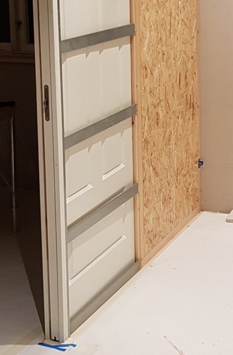 Nyinstallerad Dooria skjutdörr delvis öppen framför en oskyddad OSB-vägg, väntar på skruvar för montering.
