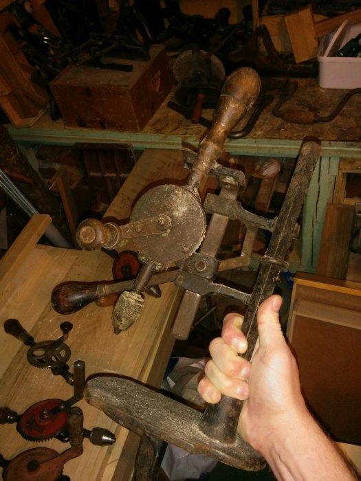 Hand håller i en gammal handdriven borrmaskin i ett verktygsbelamrat rum.