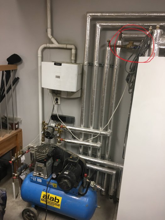 Värmesystem i ett pannrum med isolerade rör och en synlig "filterball" markerad med röd cirkel på väggen.