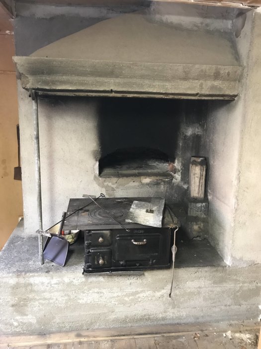 En omålad och sotig bagarstuguugn i ett torp med gamla köksredskap framför sig.