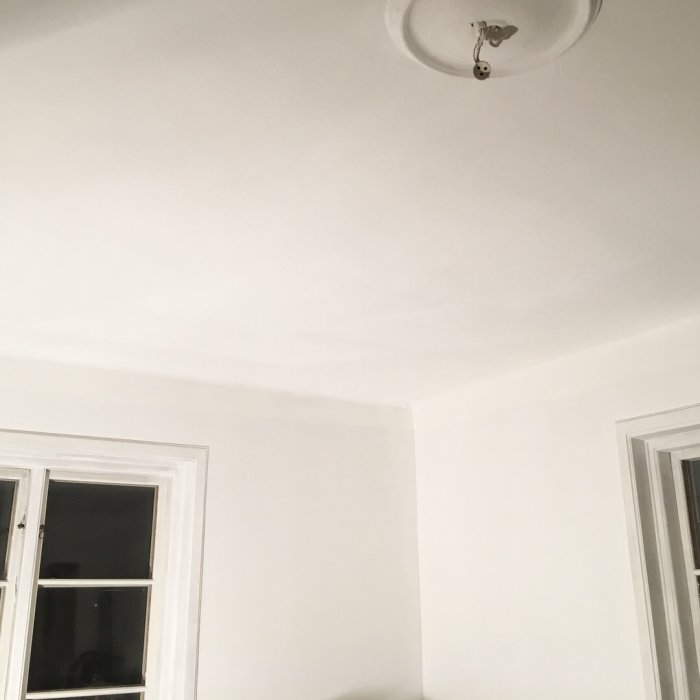 Nymålat vitt tak och väggar i rum med taklampa och fönster, ger intryck av högre takhöjd.