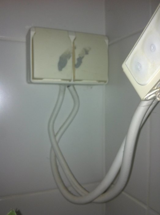 Oanvända kablar hänger från en gammal elkontakt på en kakelvägg.