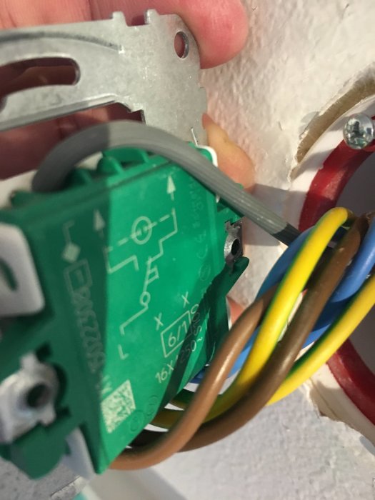 Hand håller en Plejd dosdimmer ansluten till flerfärgade elledningar i en väggbrytare.