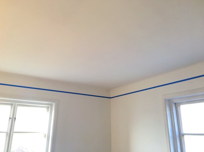 Nymålat rumstak med en markerad kant av blå tejp där takfärgen möter väggarna.