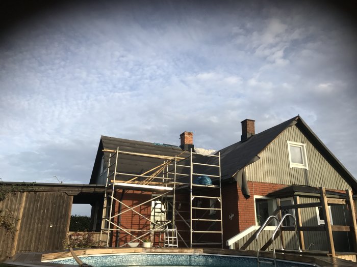 Hus under renovering med nytt takpapp och byggnadsställningar, vid sidan av en pool.