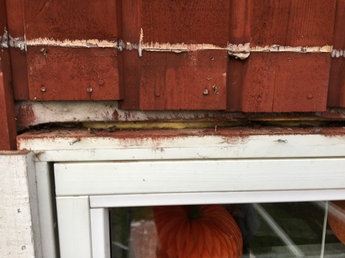 Närbild på fasad och fönster där felaktigt monterad plåt tagits bort, exponerar isolering och originalpanel.