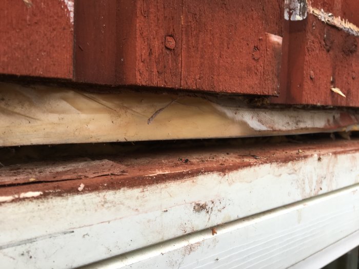Närbild av husvägg som visar felaktigt monterad plåt och lager av isolering med plast och vindtyg.
