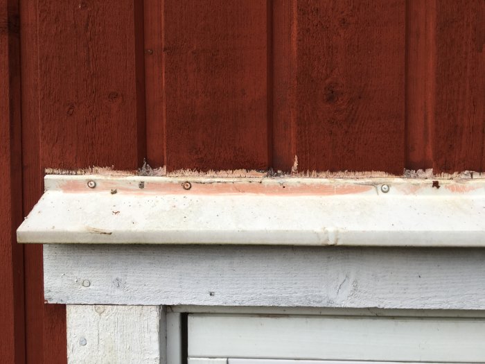 Fönsterbleck demonterat visar felaktig installation och tilläggsisolering på röd träpanel.