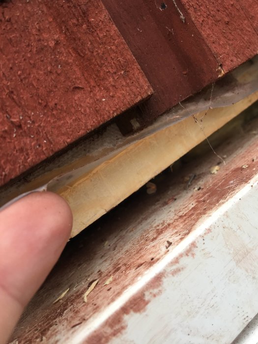 Närbild på ett hus med röd ytterpanel som visar glipor och en vit kant undertill, potentiellt relaterad till vattenskada.