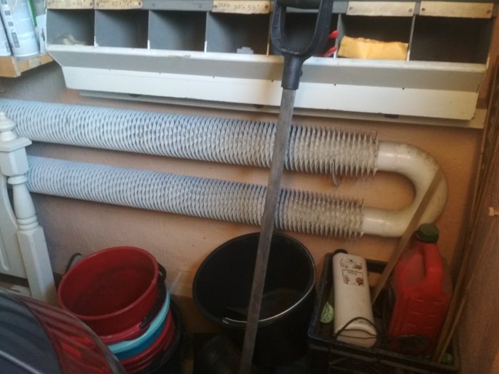 Ovanligt värmeelement med spiralmönstrade rör i ett stökigt garage, omgivet av verktyg och hinkar.