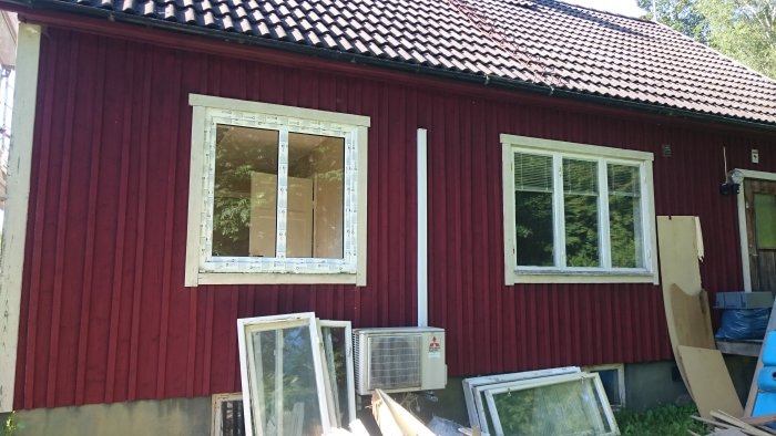 Nya fönster med synliga mätmarkeringar jämfört med ett äldre fönster, och utbytta fönster som ligger på marken framför huset.