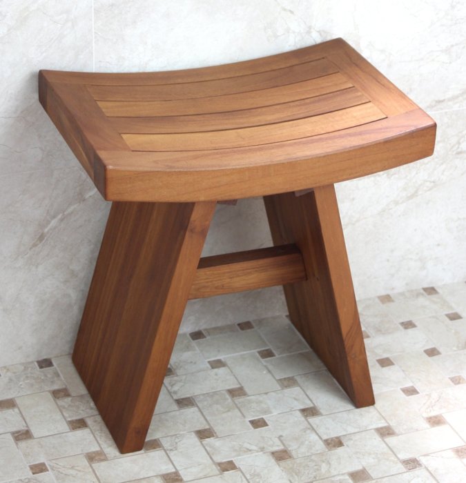 En duschpall i teak med sluttande säte placerad på ett kaklat badrumsgolv.