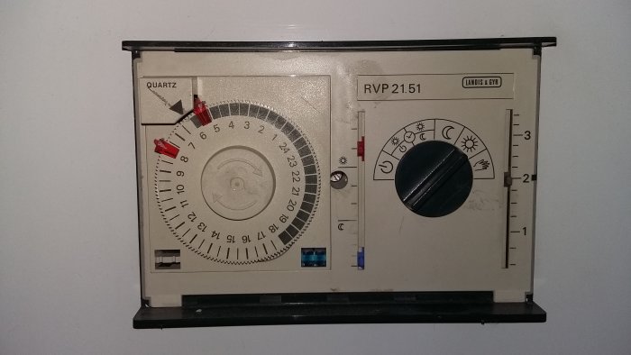 Fjärrvärmeregulator med dygnsur inställt på solen, rött och blått reglage, och temperaturinställningar.
