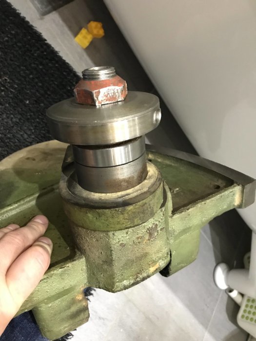 Delvis isärmonterad maskindel i skruvstäd, med en hand som håller i den och en synlig gummiklubba i bakgrunden.