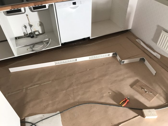 Kök under renovering med nya passbitar mellan tak och överskåp, ventilationsgaller och verktyg på golvet.