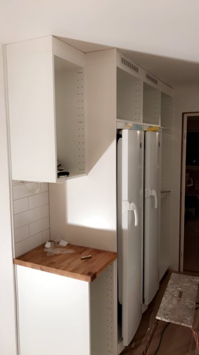 Köksinstallation med nyligen monterade passbitar mellan tak och vita skåp samt nya ventilationsgaller.