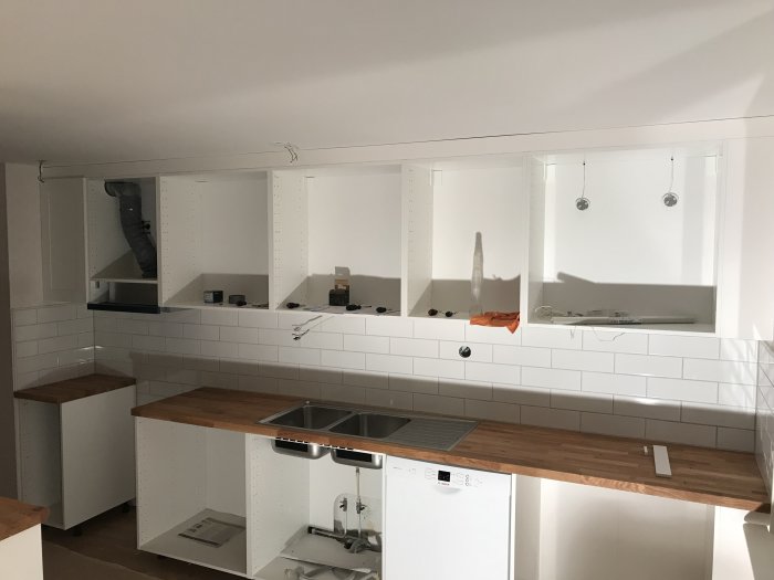 Kök under renovering med vita skåp och träbänkskivor, ventilerande galler och belysning ej färdigställt.