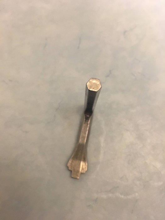 Ett slitet metallverktyg, troligen en typ av mejsel, ligger på en marmorerad yta.
