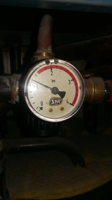 Manometer på cirka 1 bar i ett VVS-system, märkt SYR, med kopplingar och rör i bakgrunden.