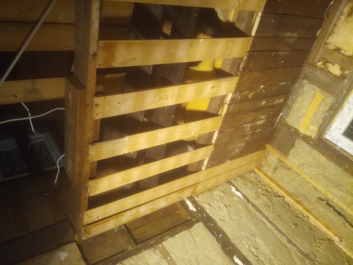 Delvis rivna träväggar och takbjälkar i ett renoveringsprojekt, med vita fläckar och en svart takbjälke.