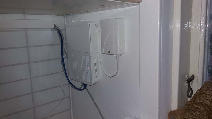 Två vita kommunikationsburkar monterade på en vägg inuti ett hus, med en blå kabel som går in i den högra burken.