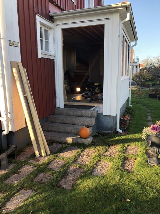 Nyinstallerad dörr i äldre rött hus med verktyg synliga inuti och en pumpa på trappan.