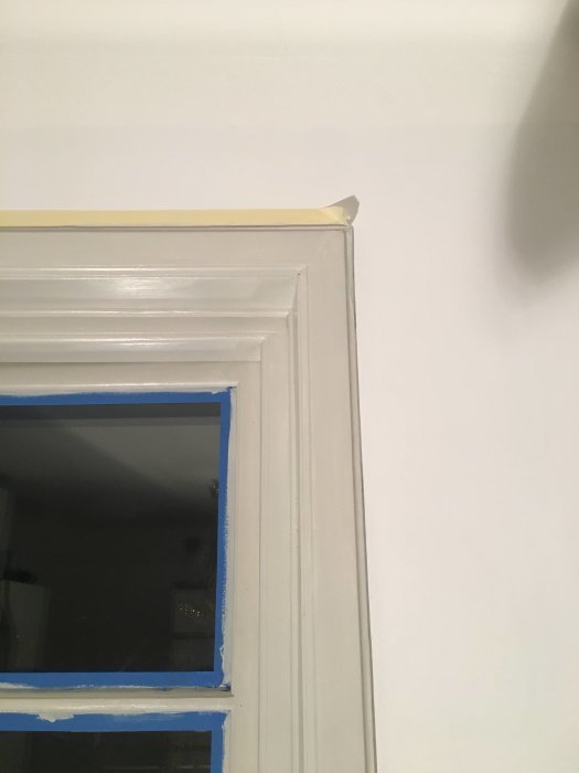 Nymålat fönster med grå-beige färg och blått skyddstejp runtom.