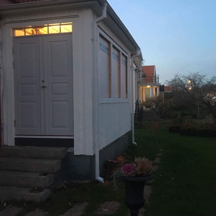 Nyinstallerad vit ytterdörr på en veranda med innertakbelysning i skymningsbelysning, verandan byggnad till ett hus.