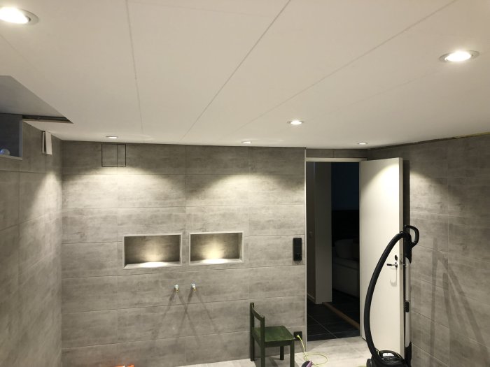 Modern renoverad källare med infällda spotlights, väggnischer med mysbelysning och termostat på väggen.