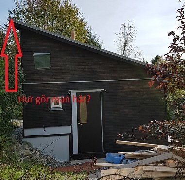 Ett halvfärdigt gästhus med svart snedtak och pappbeklädnad, synliga byggmaterial i förgrunden.
