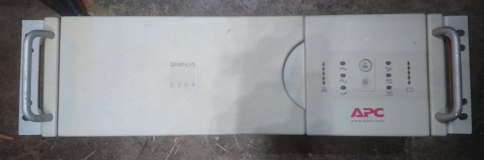 En APC Smart-UPS 2200-enhet utan fungerande batterier ligger på ett golv.