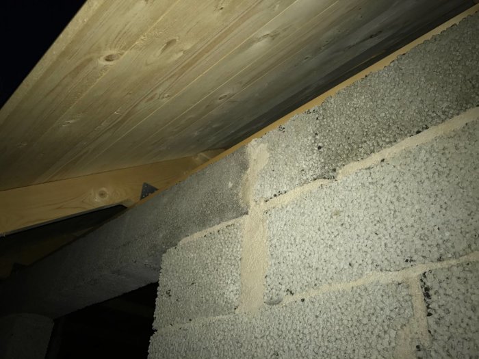 Detaljbild av ett hörn av ett murat lecahus med takstolar och limträbalk synlig, redo för putsning.