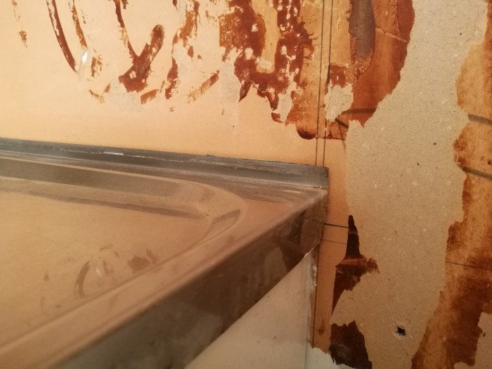 Vägg vid diskbänk med rester av gammalt kakel och synlig klack som skapar ett hålrum inför ny kakelsättning.