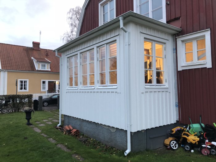 Nyinstallerade fönster i ett ljusmålat hörn av ett rött trähus, ger utsikt och ljus till entrén.