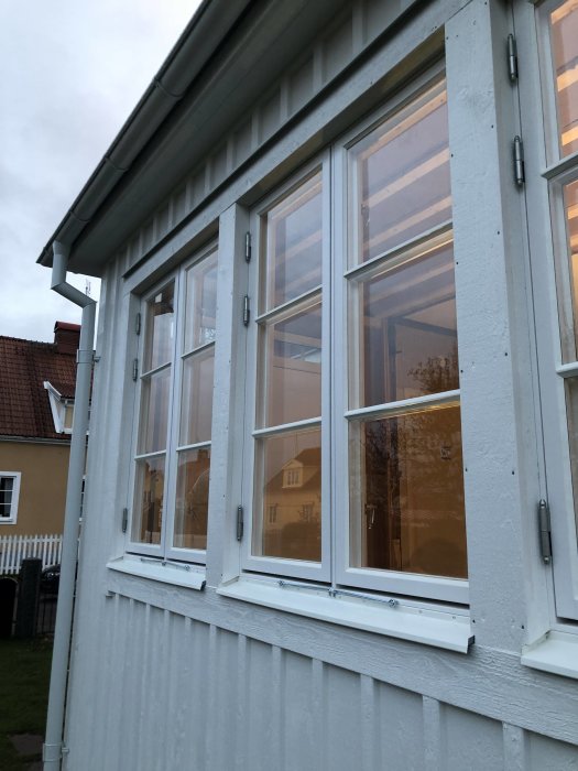 Nyinstallerade vita fönster på en ljusgrå träfasad med synlig utsikt av omgivningen.