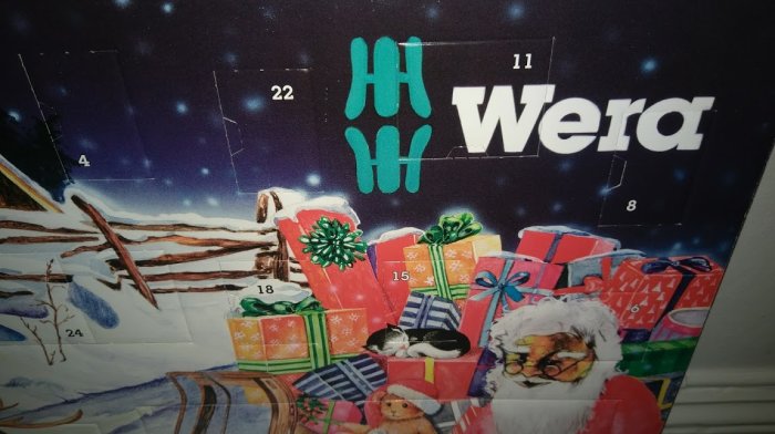 Julkalender med Wera-logga, tomte och högar av färgglada paket i snölandskap.