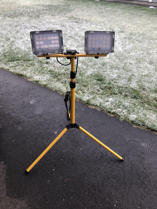 Dubbla LED-strålkastare monterade på ett gult stativ i ett snöfläckigt gräslandskap.