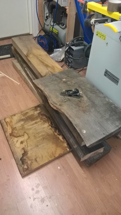 Ekplankor i olika storlekar ordnade på en verkstadsgolv med en handsåg, förberedelse för klaffbordstillverkning.