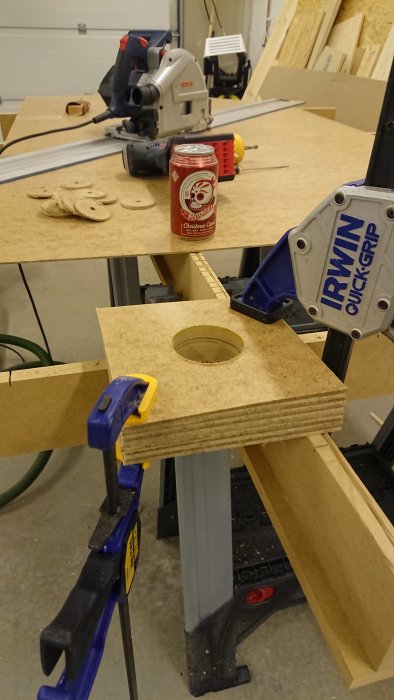 Verkstadsarbete med sågade spot-skivor, klämma, och burk julöl på arbetsbänken.