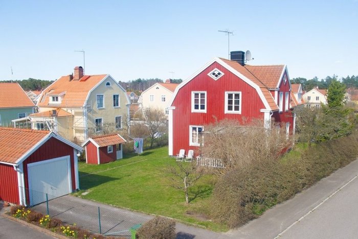 Rött trähus från 1930 med vitmålade fönster och tegeltak, kallgarage till vänster, omgivet av gröna gräsmattor.