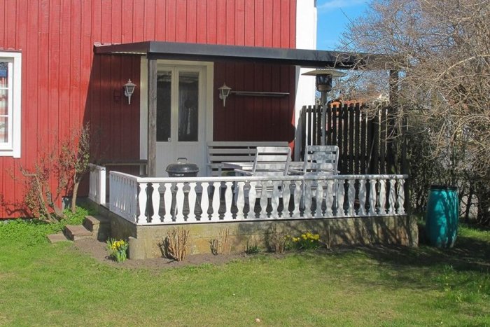 Rödfärgat hus med vita knutar, veranda med vitt räcke och utemöbler, byggt 1930, renoverat på 1950-talet.