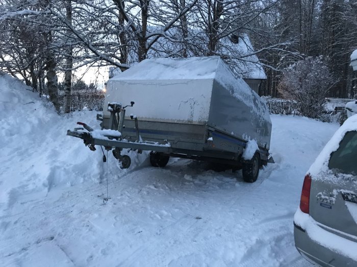 Släp lastat med kompostbetong i snöig uppfart vid skymning, lågt kultryck indikerat.