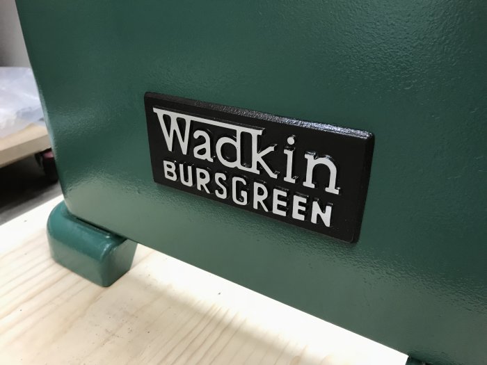 Del av en grönmålad såg med en svart logotypplåt för "Wadkin Bursgreen," indikation på en renoveringsprocess.