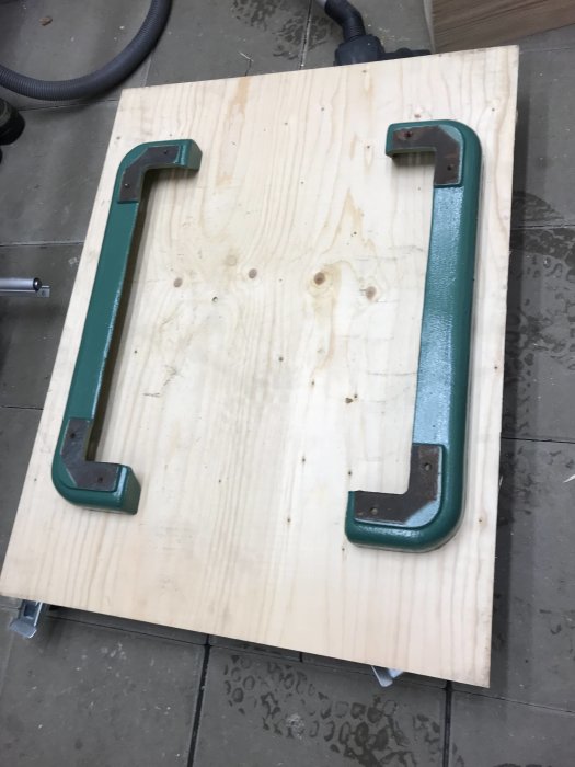 Nyfärgade gröna metallhandtag som ligger på en plywoodskiva.